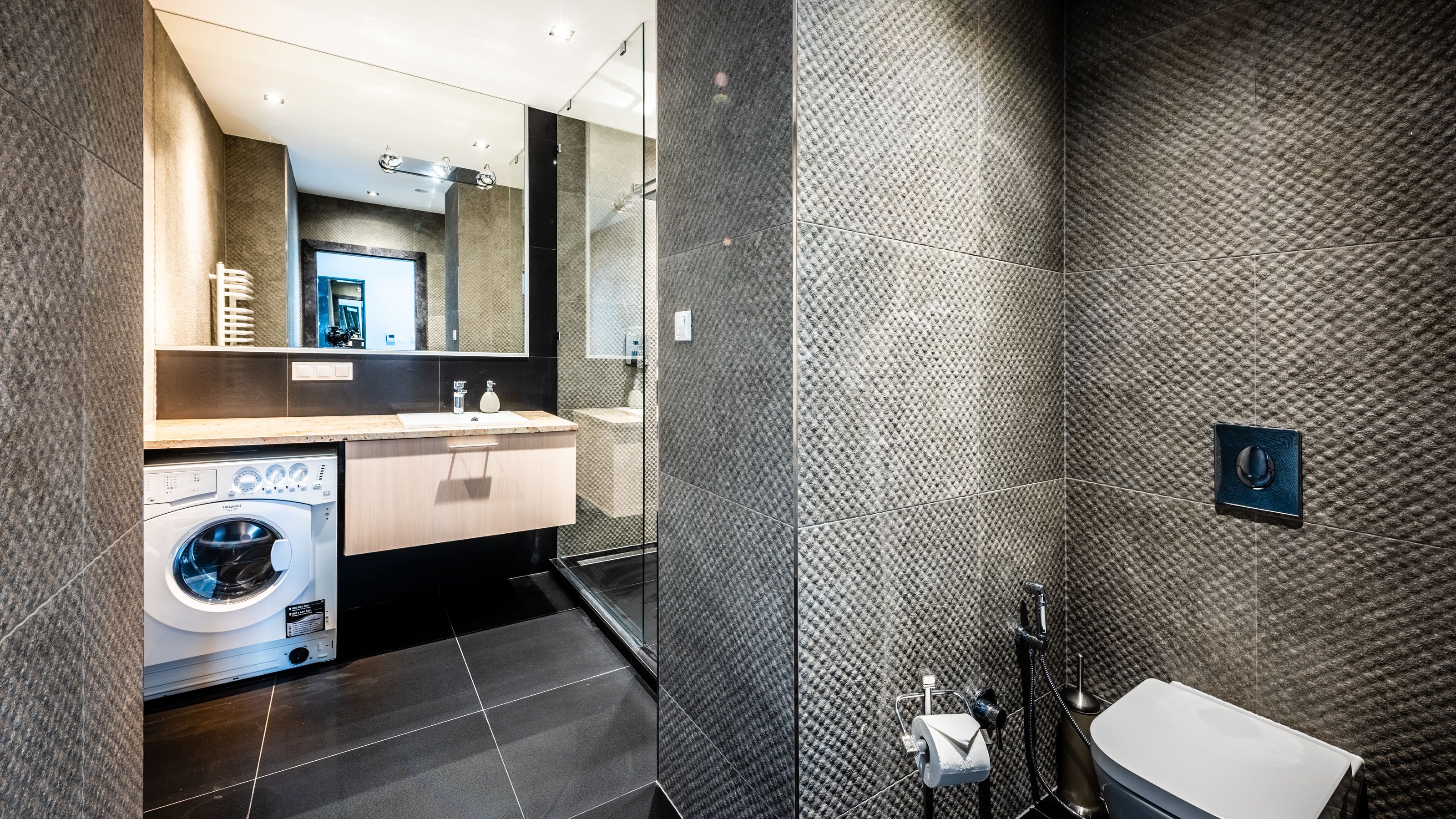 A modern bathroom with a built-in washing machine, a large mirror, and a bathtub.