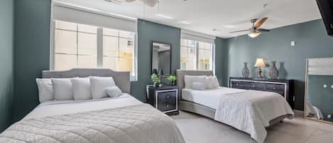 A modern hotel room with two beds, a ceiling fan, large windows, and a nightstand with decorative items.