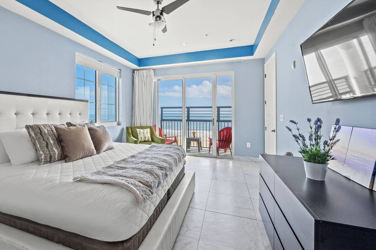 Ein Schlafzimmer mit einem großen Bett, einem Deckenventilator und Blick auf den Strand durch die Schiebetüren.