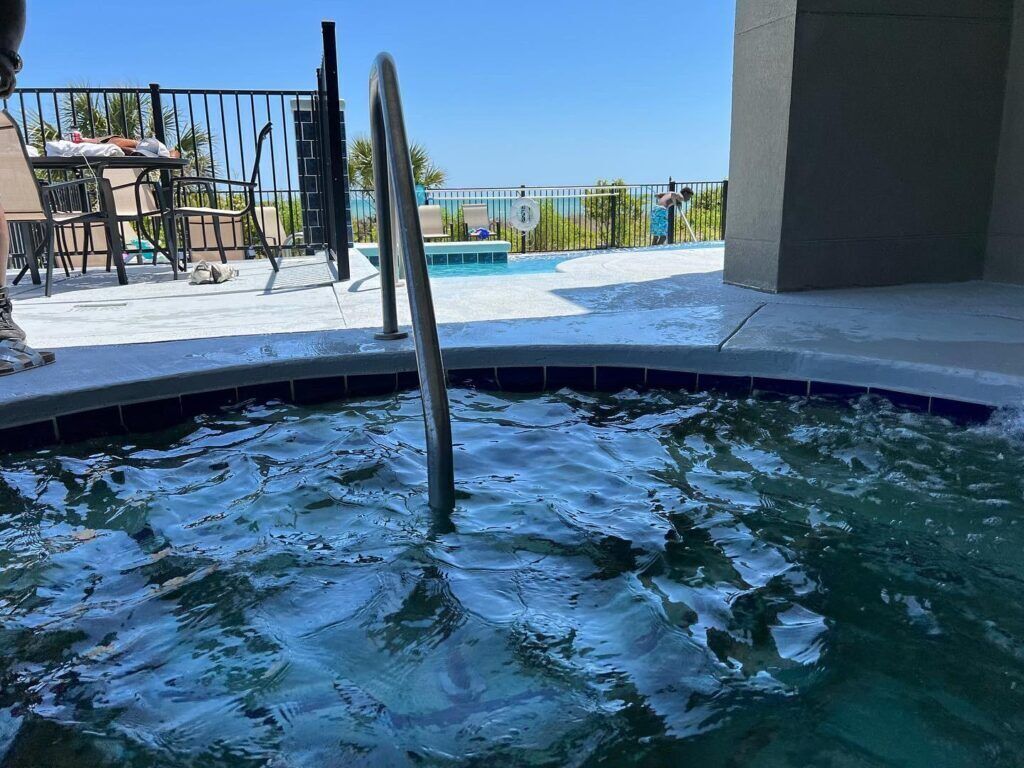 En swimmingpool med en metalstige, et bord og stole, og havudsigt.