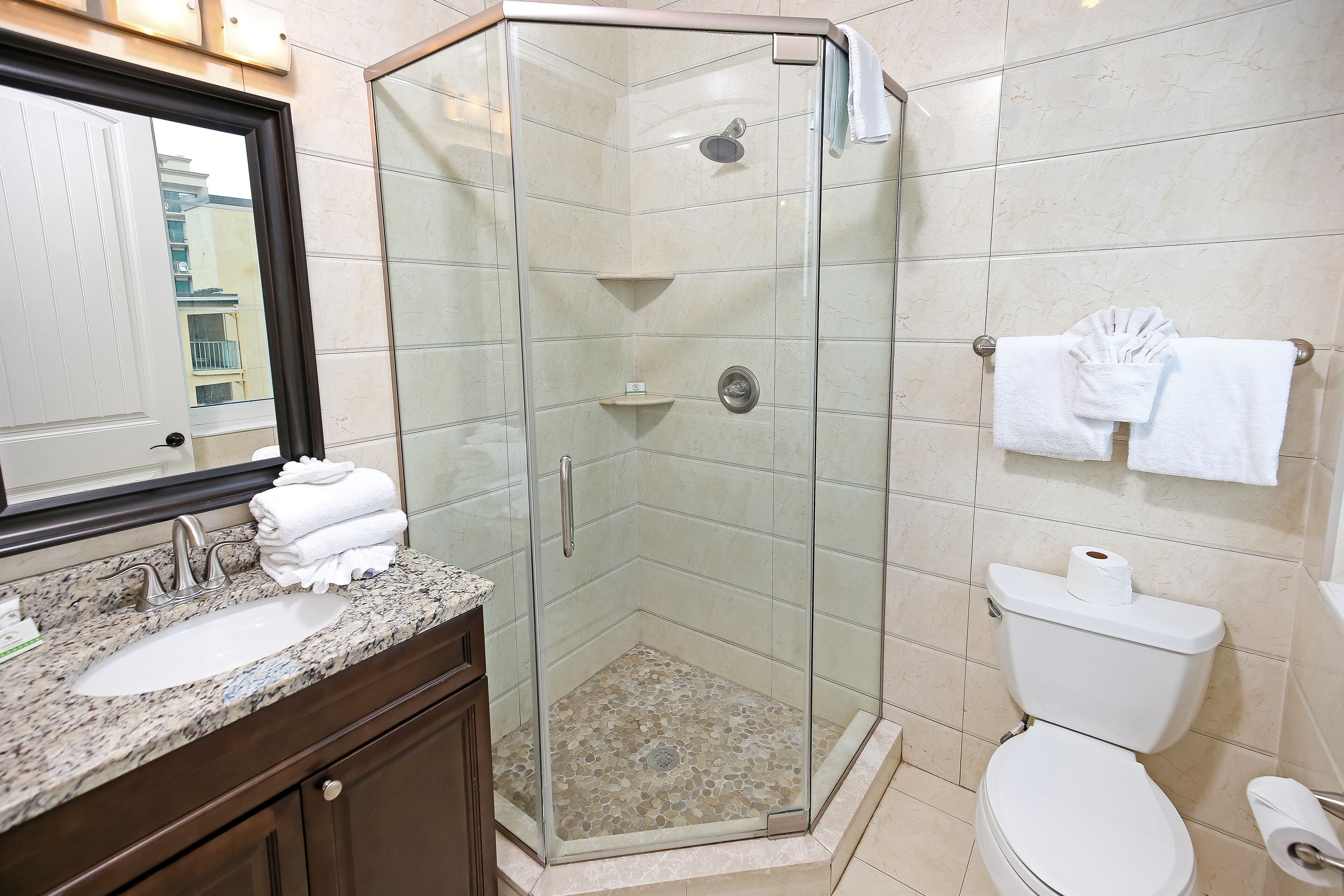 A bathroom with a glass-enclosed shower, a sink with a marble countertop, and a toilet.