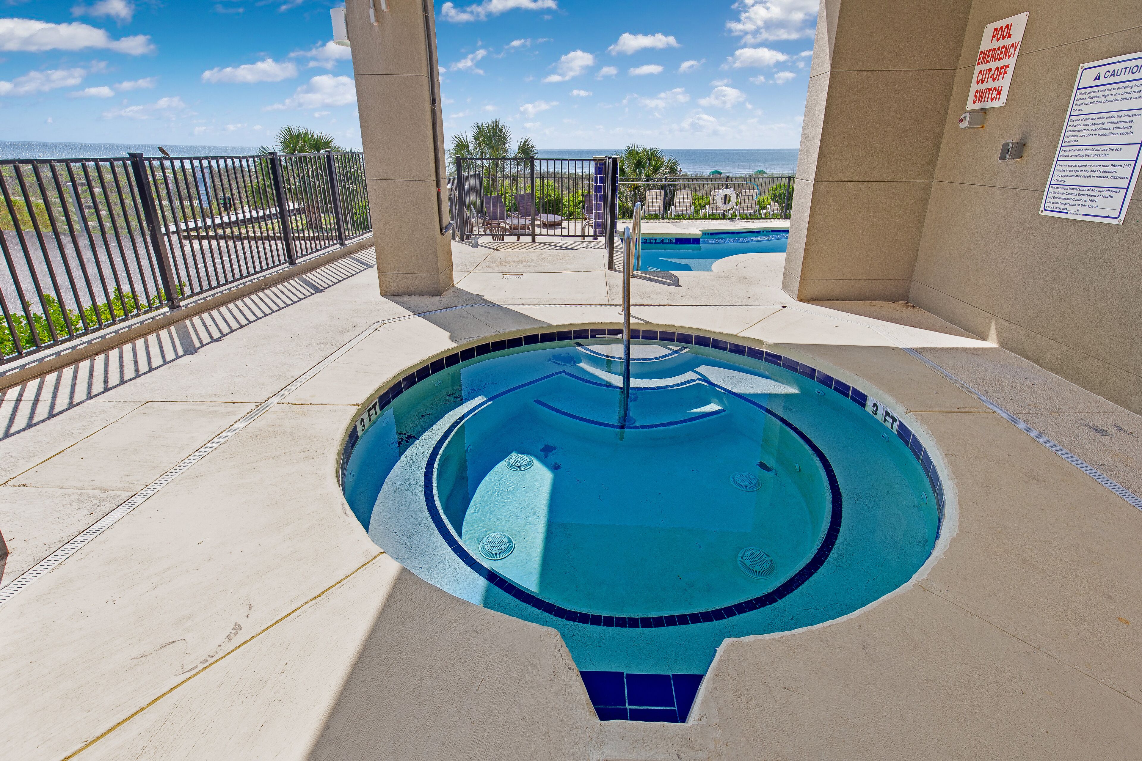 A swimming pool with a safety sign, a pool emergency cut-off switch, and a view of the ocean.