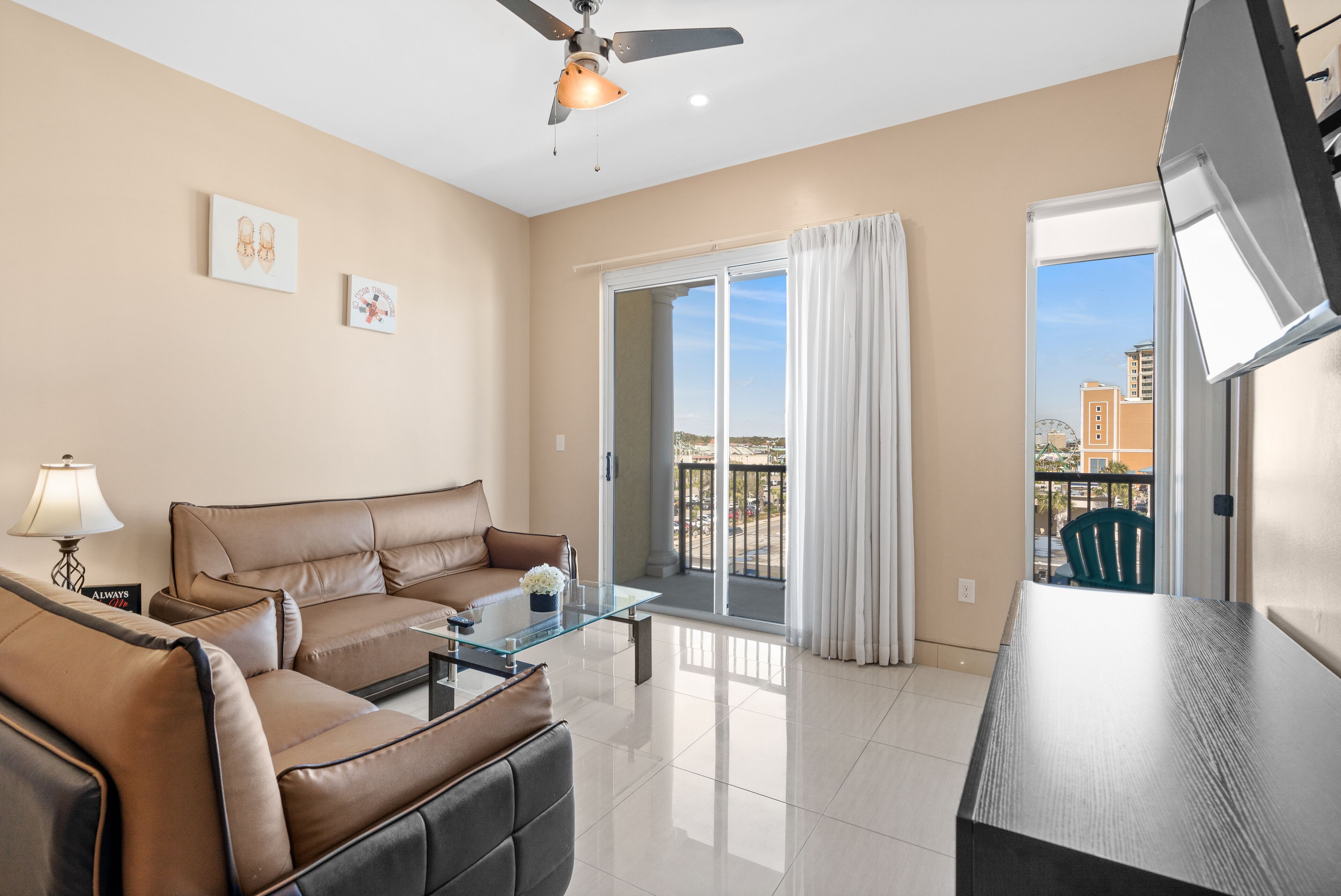 A modern living room with a sofa, coffee table, and a balcony with a view of buildings and a Ferris wheel.