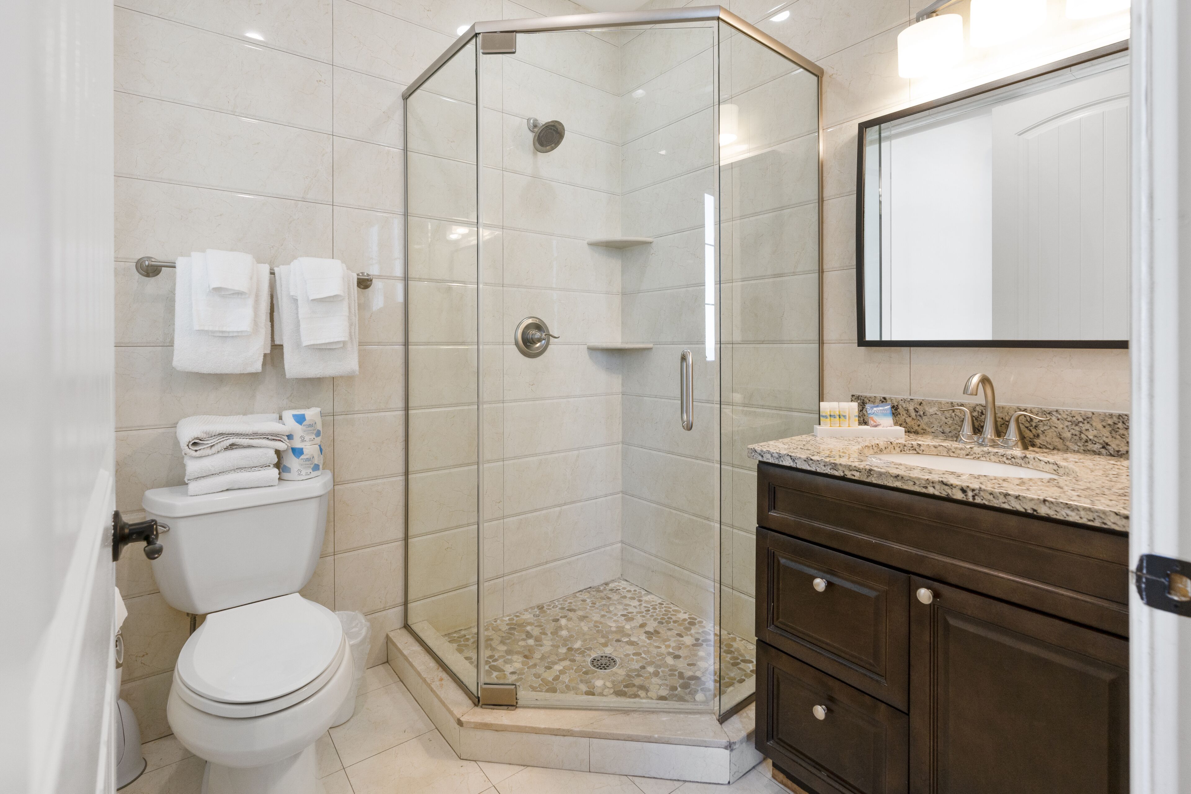 Un baño moderno con cabina de ducha acristalada, inodoro y tocador con lavabo y espejo.