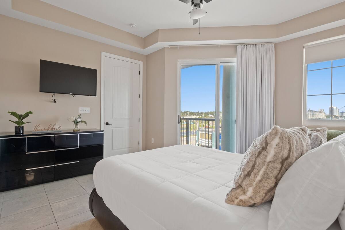 Ein Hotelzimmer mit einem großen Bett, einem an der Wand befestigten Flachbildfernseher, einem Schminktisch und einem Balkon mit Blick auf die Stadt.