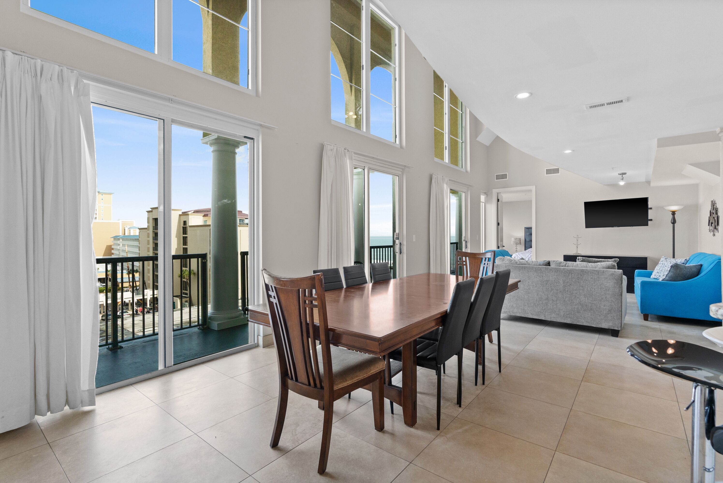 A spacious living area with a dining table, sofas, and a balcony with a view of the city.