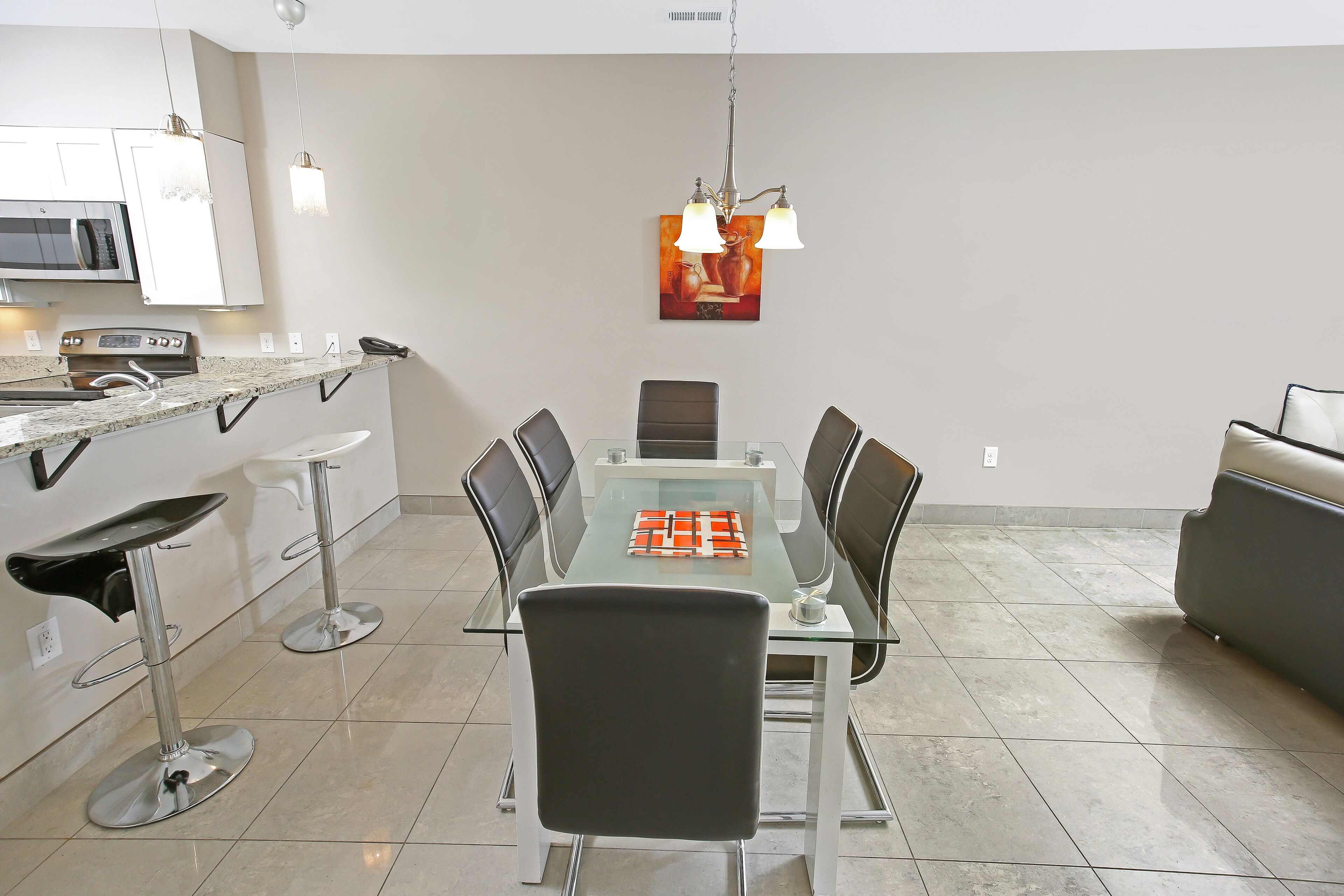 A modern kitchen with white cabinets, a microwave, and a gas stove. There is a dining area with a glass table and black chairs.