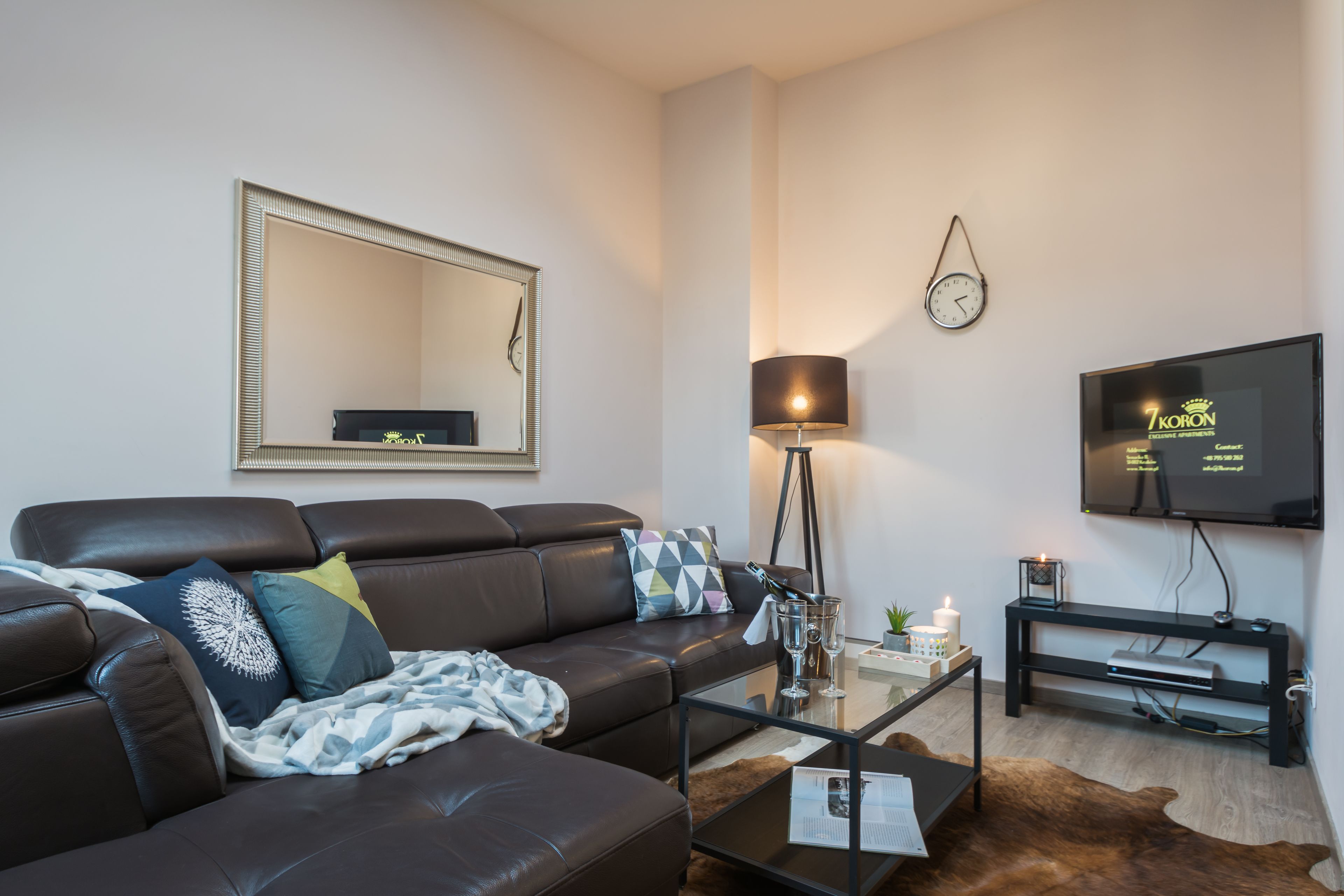 A modern living room with a leather sofa, a coffee table, a flat-screen TV, a lamp, and a clock on the wall.
