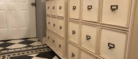 A hallway with a checkered floor, a white door, and a row of cream-colored storage cabinets with black handles.