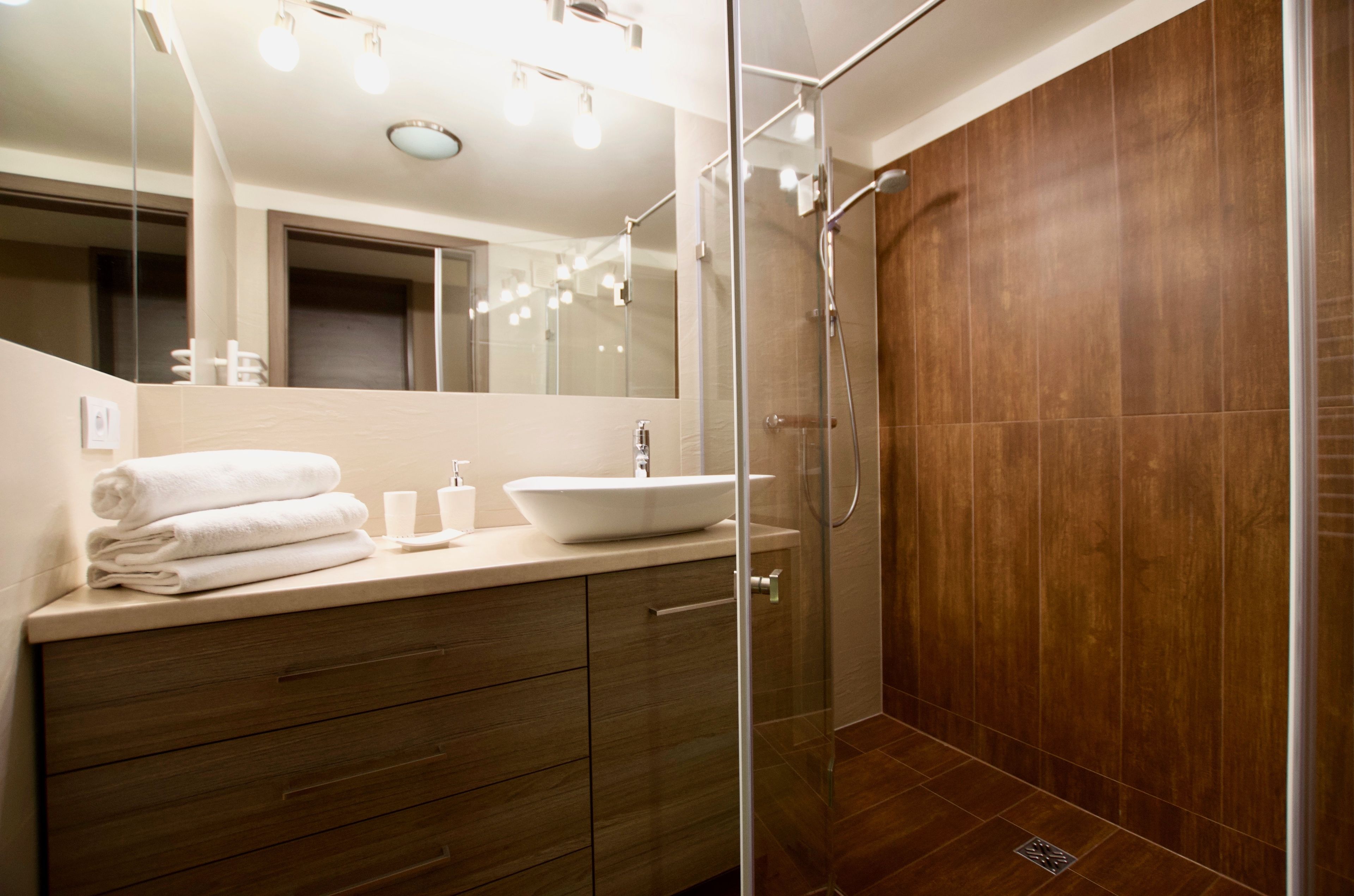 A modern bathroom with a glass shower enclosure, a wooden vanity, and a large mirror.