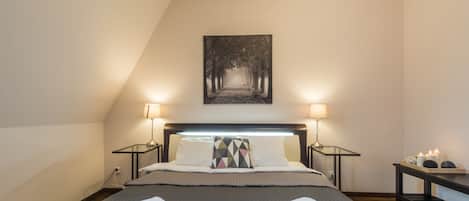 A neatly made bed with two rolled towels, a bedside table with a lamp, and a wall-mounted picture.