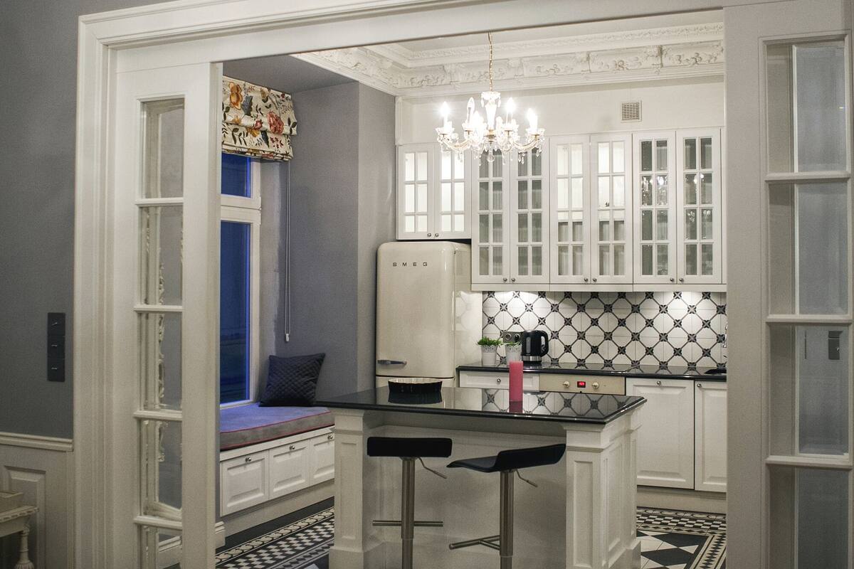 Una cocina con armarios blancos, piso a cuadros blanco y negro, y una araña.