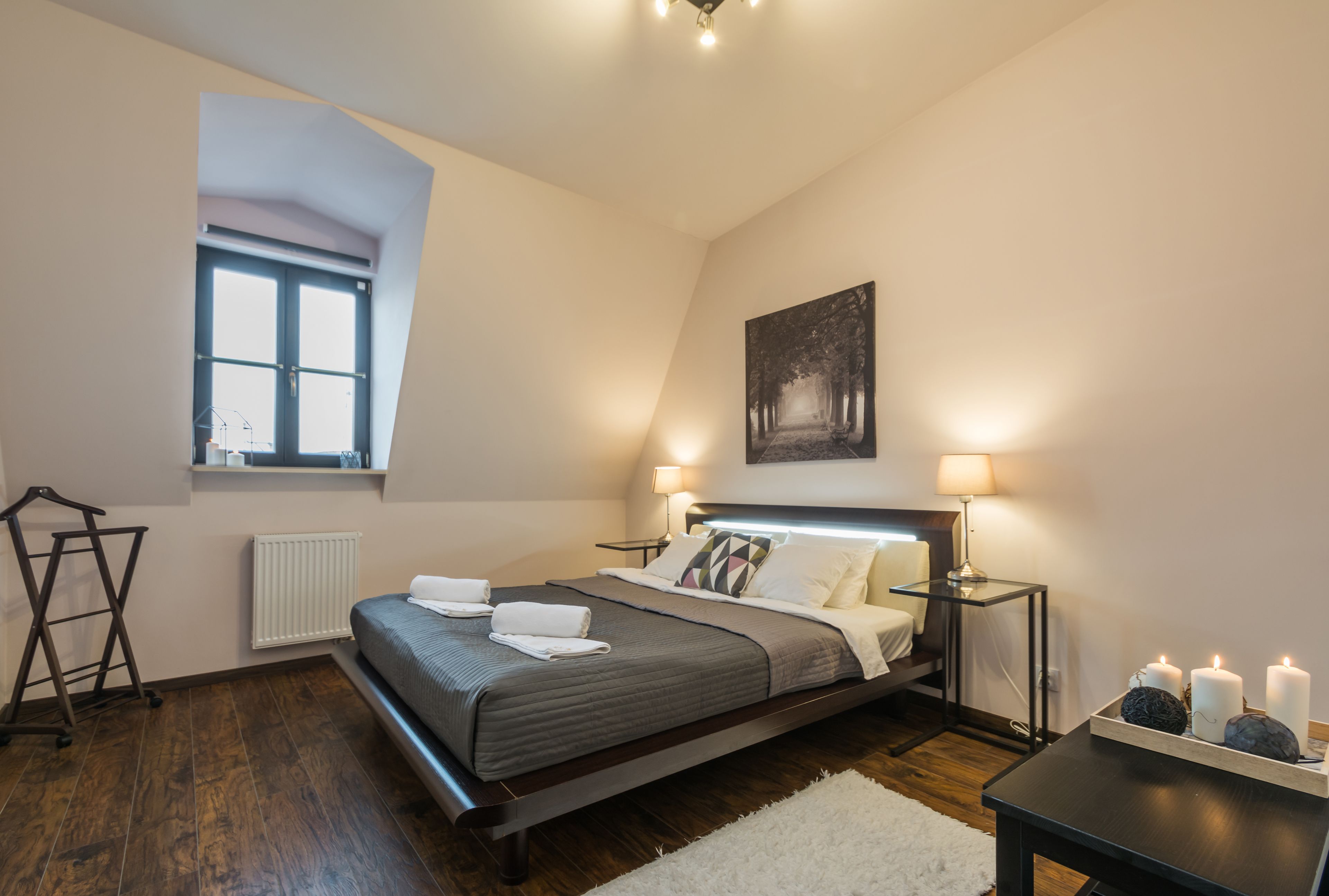 A modern bedroom with a large bed, a window, a radiator, a hanging light fixture, and a painting on the wall.