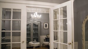 A room with a chandelier, a white cabinet, a small table, and a chair.