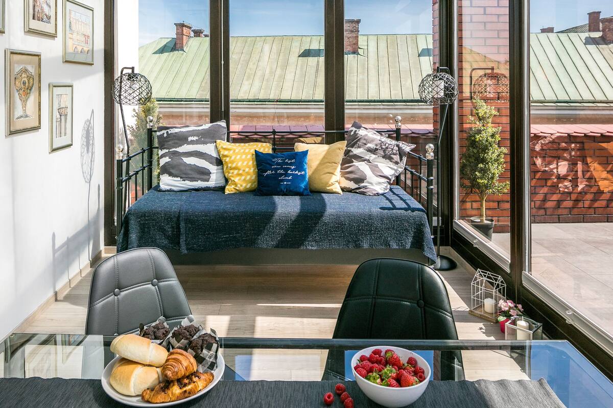 Una habitación moderna con una mesa de vidrio, un sofá con cojines de colores y vistas a edificios a través de grandes ventanales.
