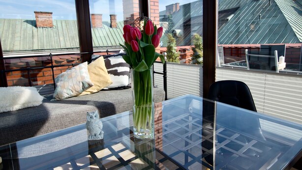 A glass table with a vase of tulips, a sofa with cushions, and a view of buildings through a window.