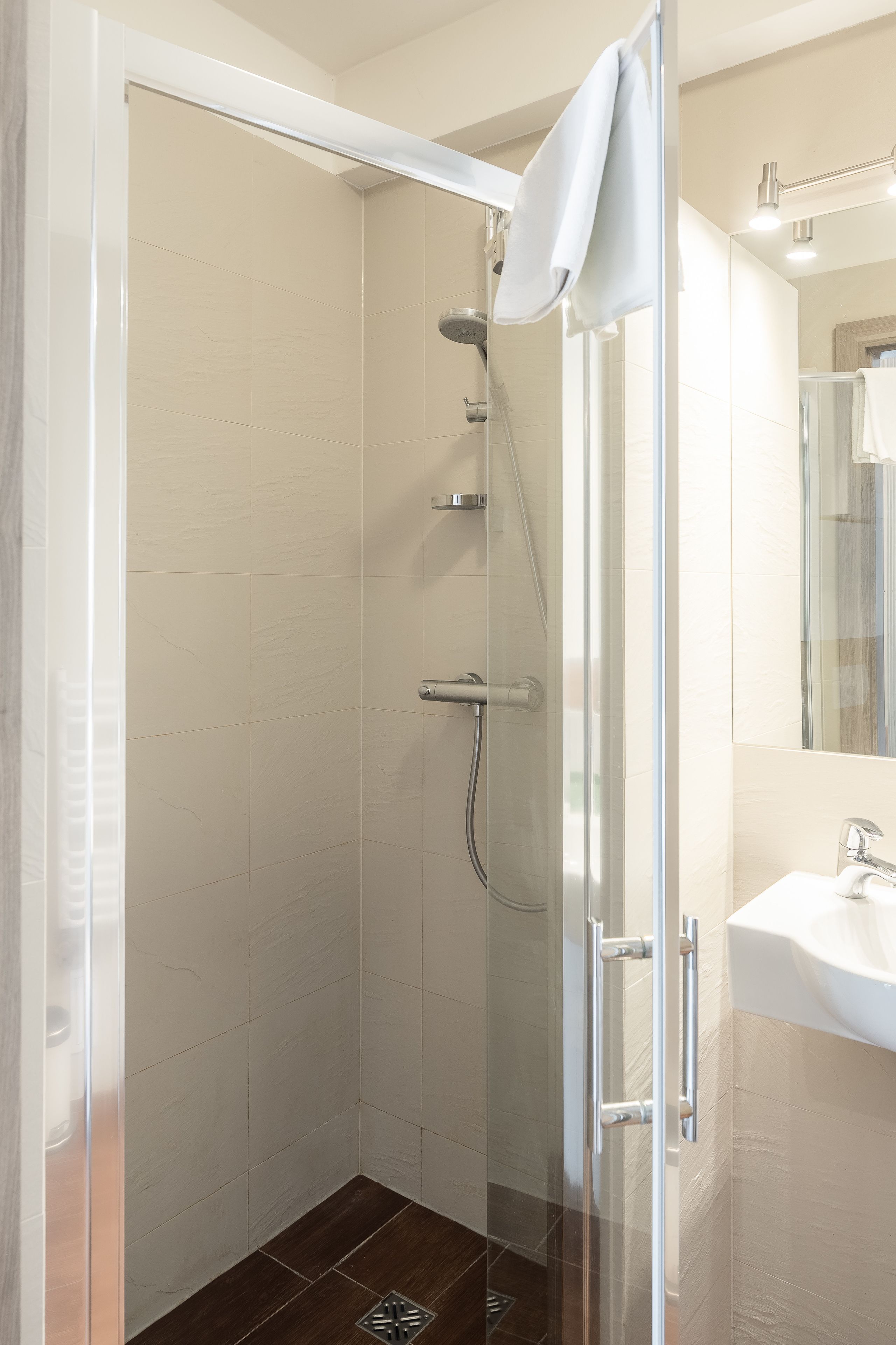 A modern bathroom with a glass-enclosed shower, a white sink, and a mirror above the sink.