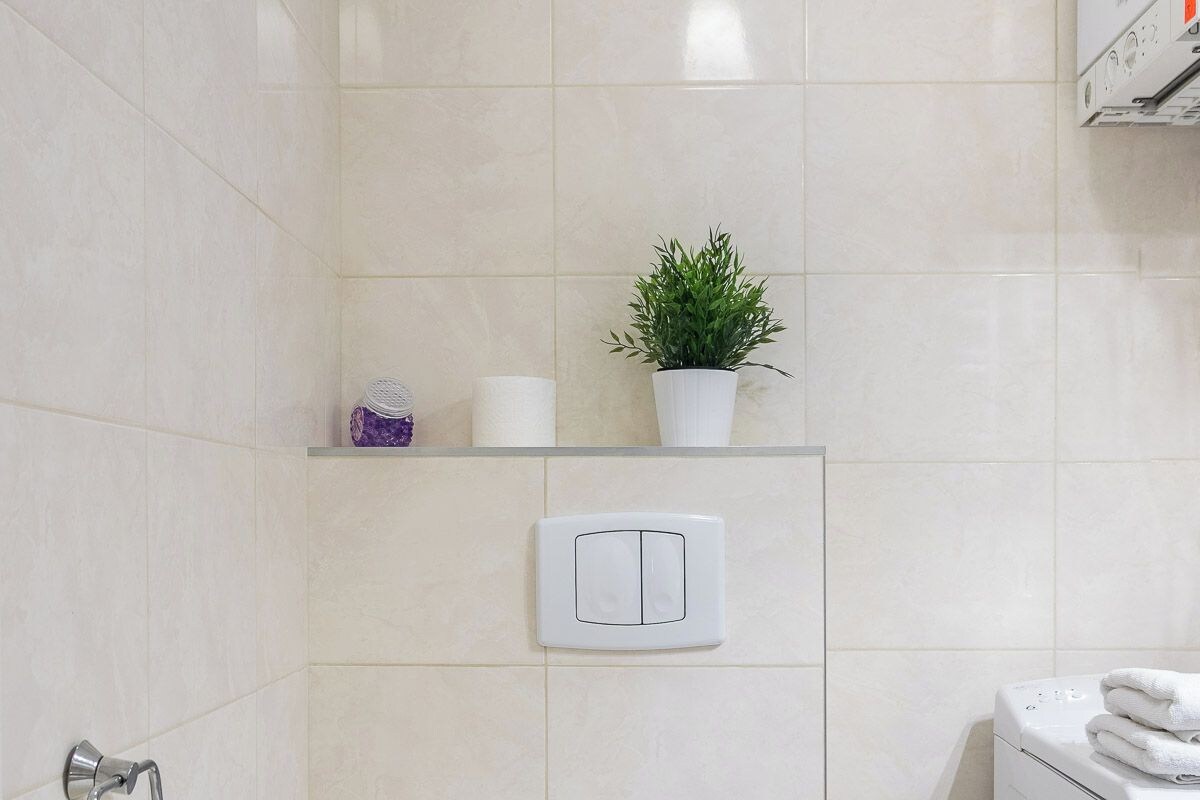 A modern bathroom with a toilet, a shelf with a plant, and a washing machine.