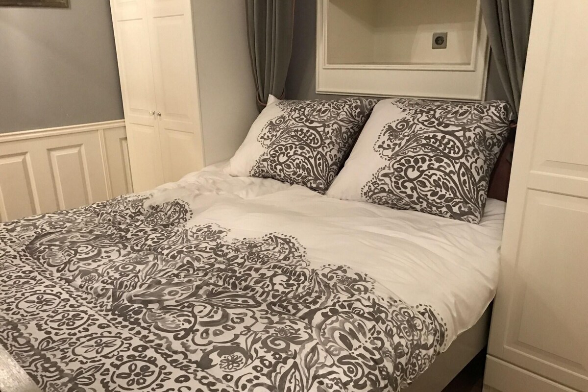 A bed with a patterned bedspread and two pillows, a white headboard, and a door to the left.