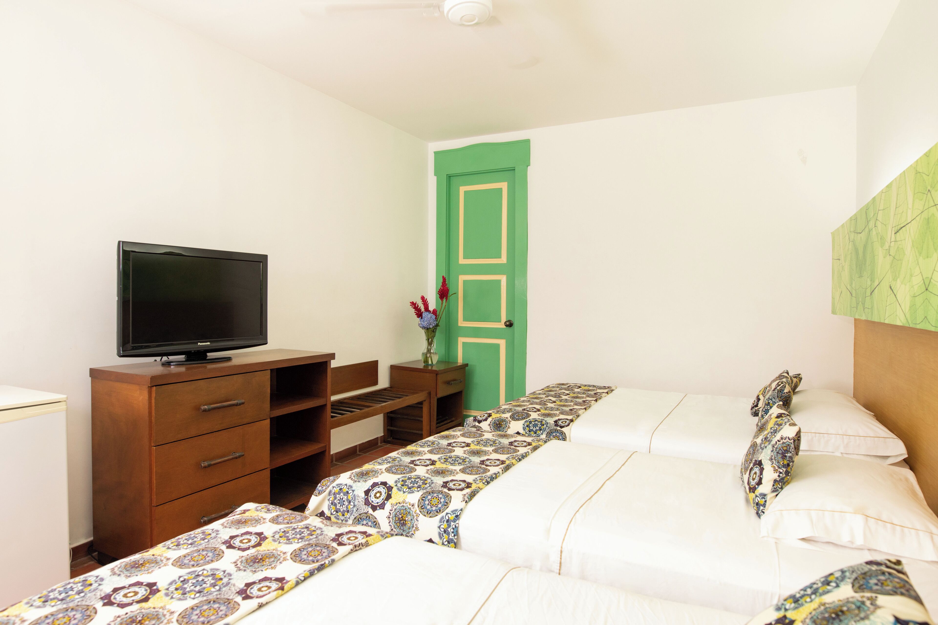 A bedroom with two beds, a television on a wooden dresser, and a green door.