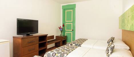 A bedroom with two beds, a television on a wooden dresser, and a green door.
