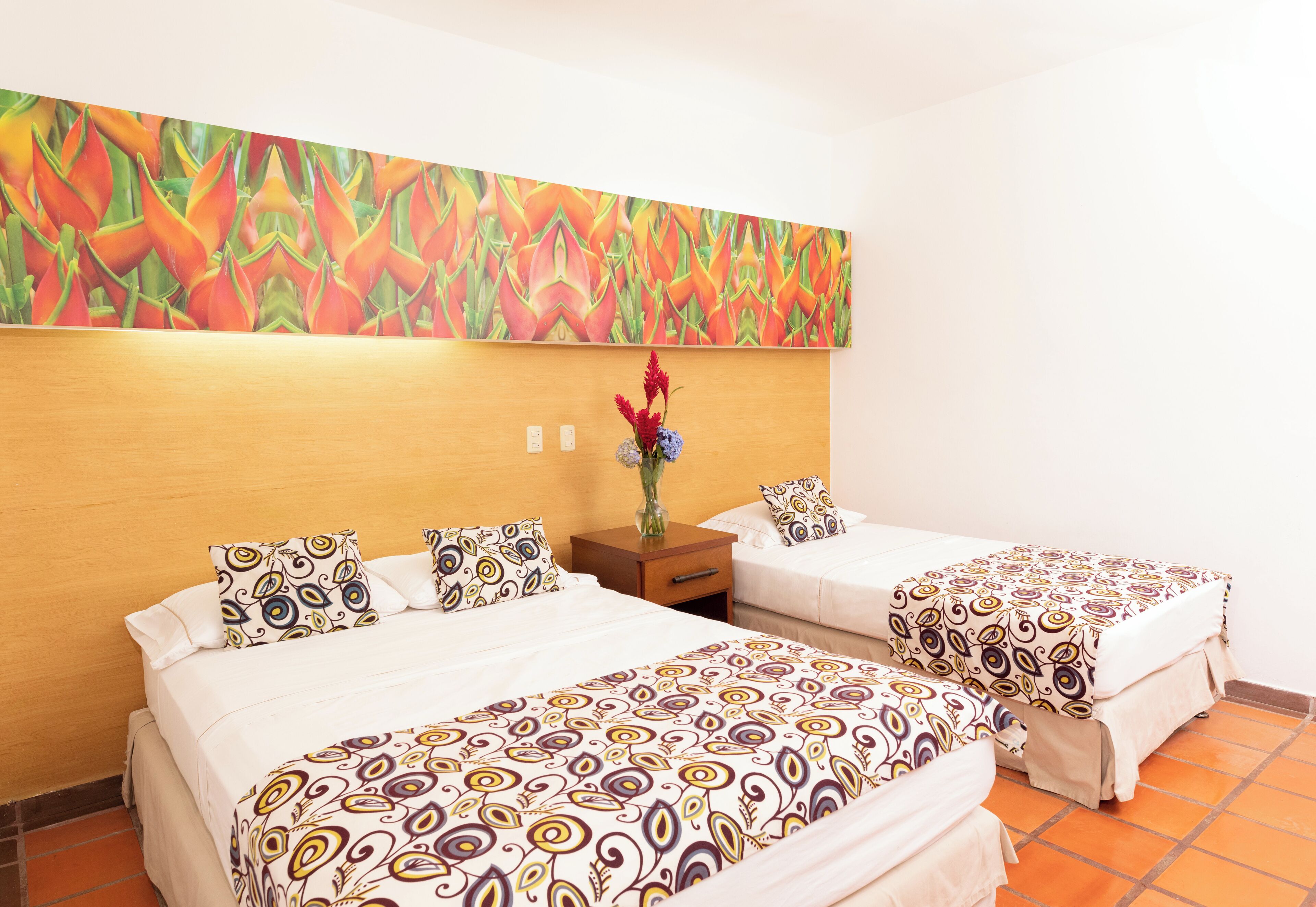A hotel room with two beds, a wooden headboard, a nightstand, and a colorful abstract painting above the beds.
