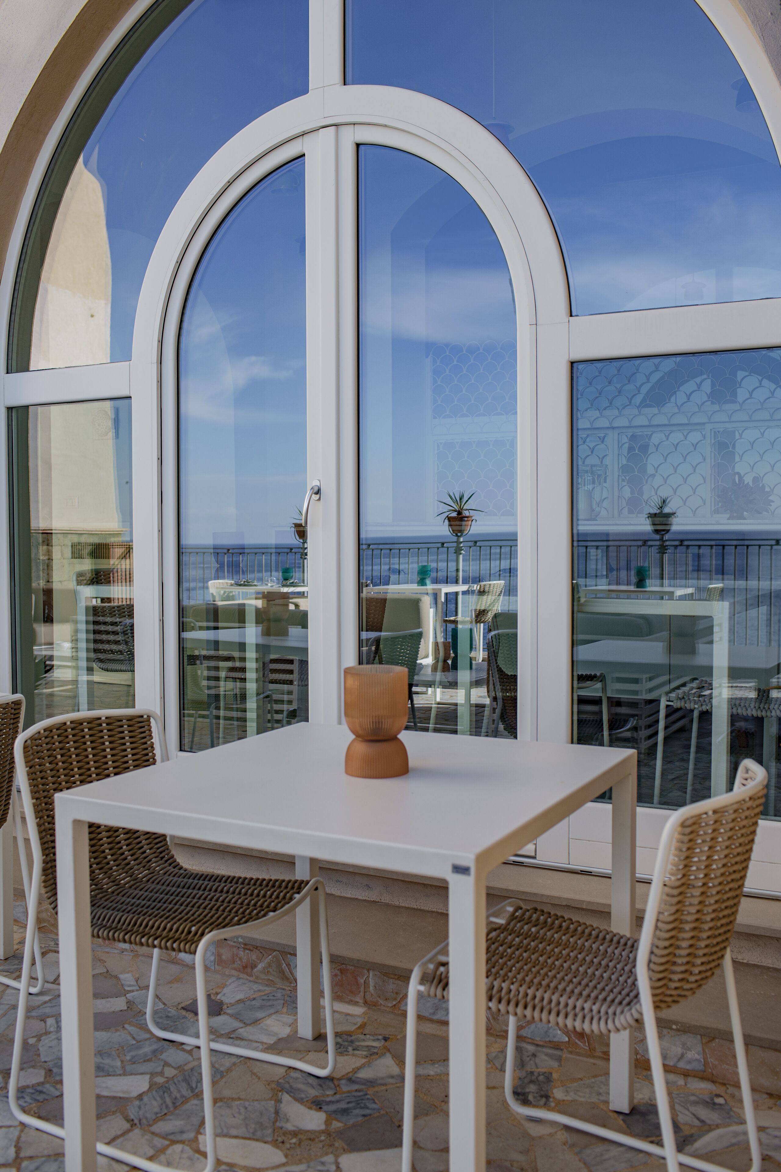 A terrace with a white table and wicker chairs, overlooking a scenic view.