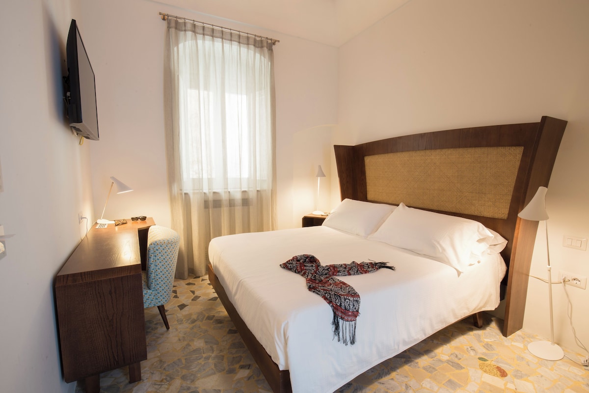 Een hotelkamer met een bed, nachtkastjes, een bureau, een stoel, een televisie en een raam met gordijnen.