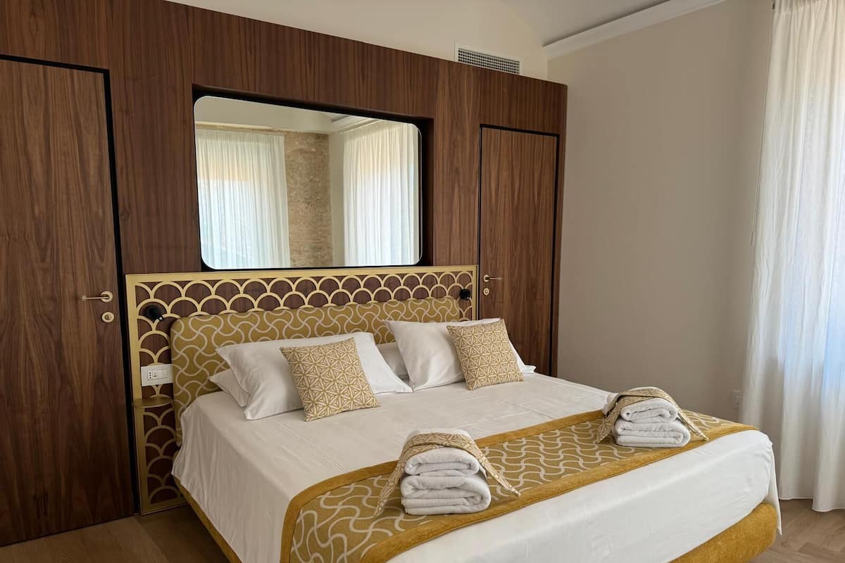 A hotel room with a large bed, wooden wardrobe, and a mirror above the bed.