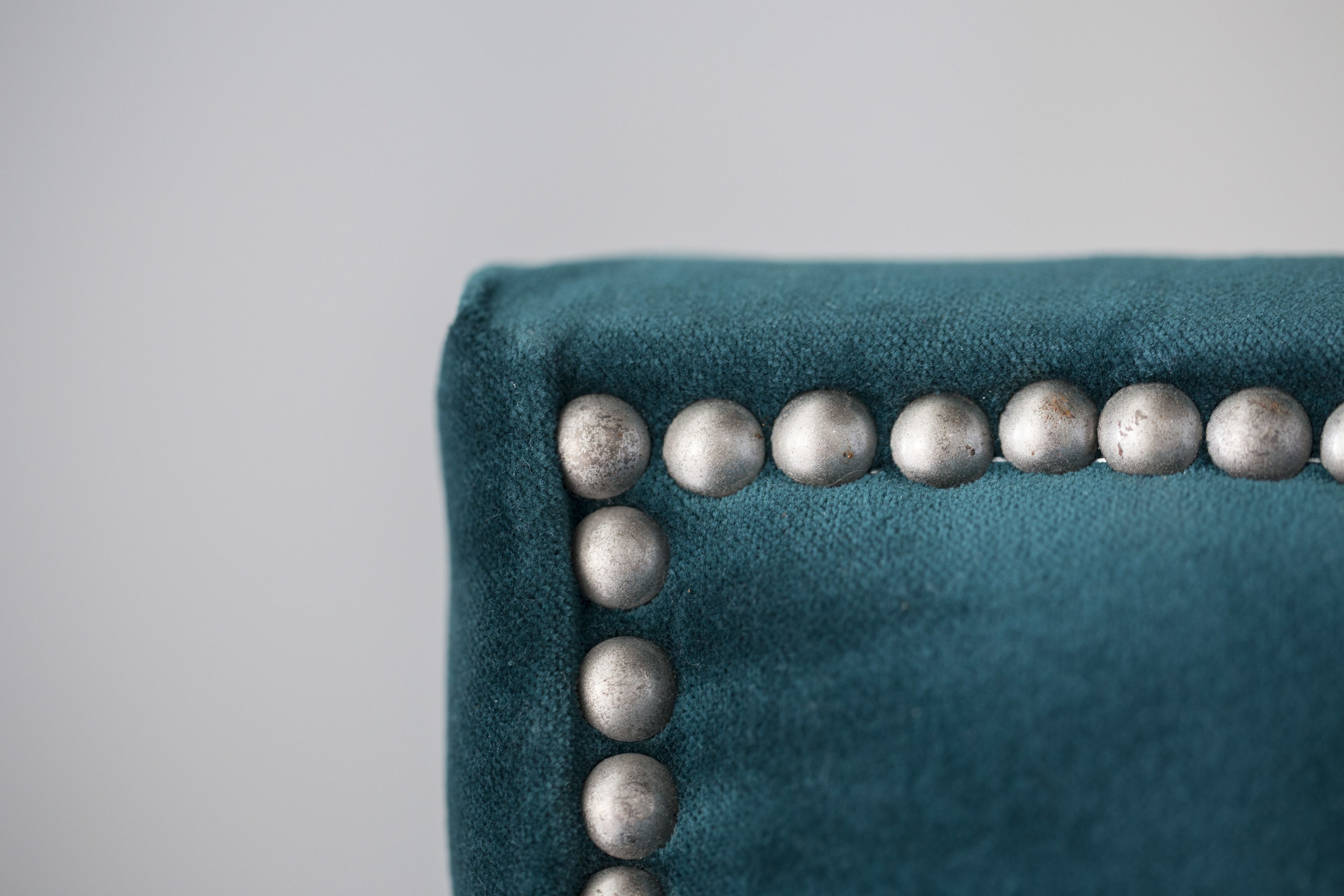 A close-up of a teal upholstered chair with a row of metallic spherical buttons along the edge.