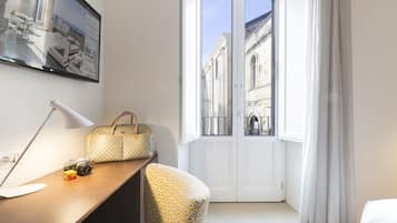 Quarto de hotel com escrivaninha, cadeira, bolsa, câmara e vista para um edifício através de uma porta.