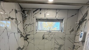 A bathroom with marble walls, a window, a hand dryer, and a tiled floor. - Immokalee Inn (Immokalee)