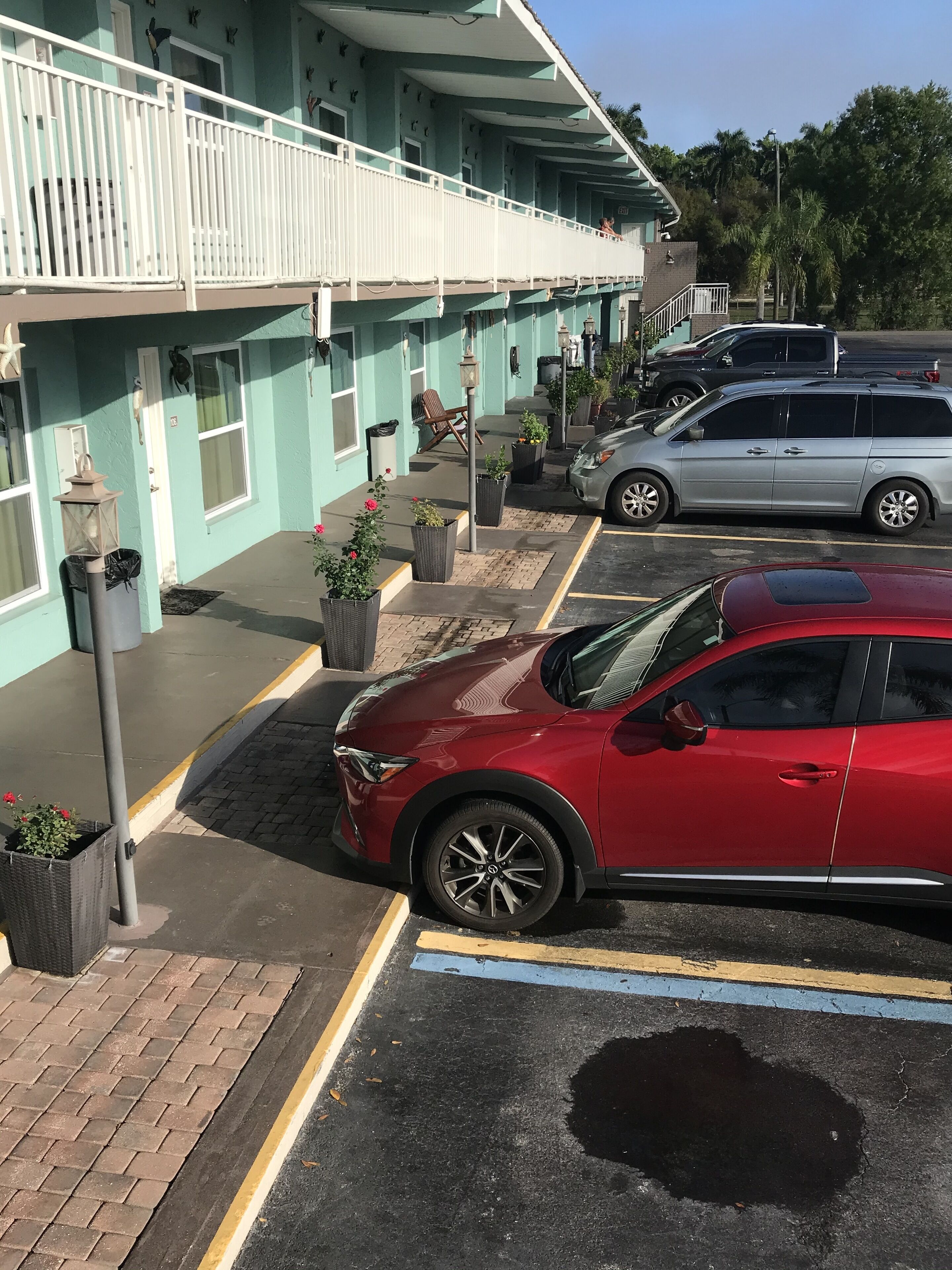 Un immeuble à la façade bleu clair, doté d’un balcon blanc et comprenant un espace de stationnement où se trouve une voiture rouge.