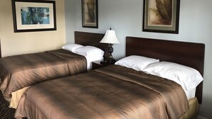 A hotel room with two beds, a nightstand with a lamp, and three framed artworks on the walls. - Immokalee Inn (Immokalee)