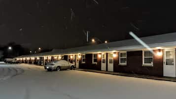 A motel with a row of rooms, each with a door and windows, and a covered parking area with a car.