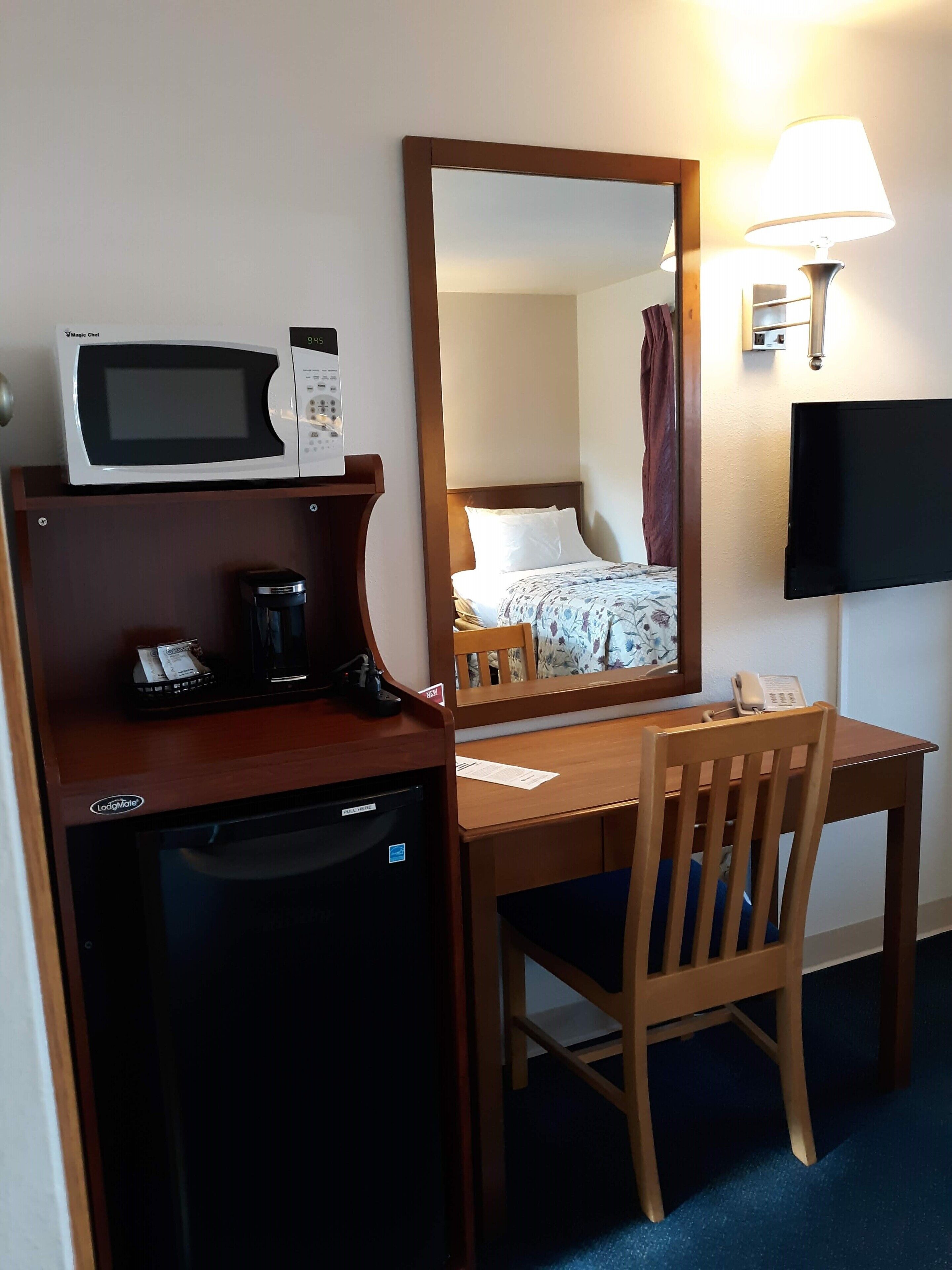 A hotel room with a desk, a microwave, a coffee maker, a telephone, and a television.