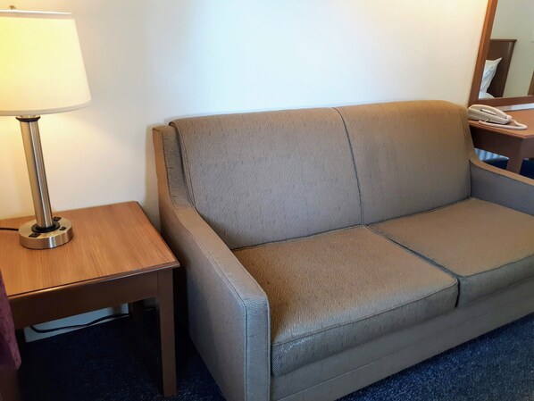 A beige sofa with a textured pattern, a wooden side table with a lamp, and a telephone on a wooden surface.