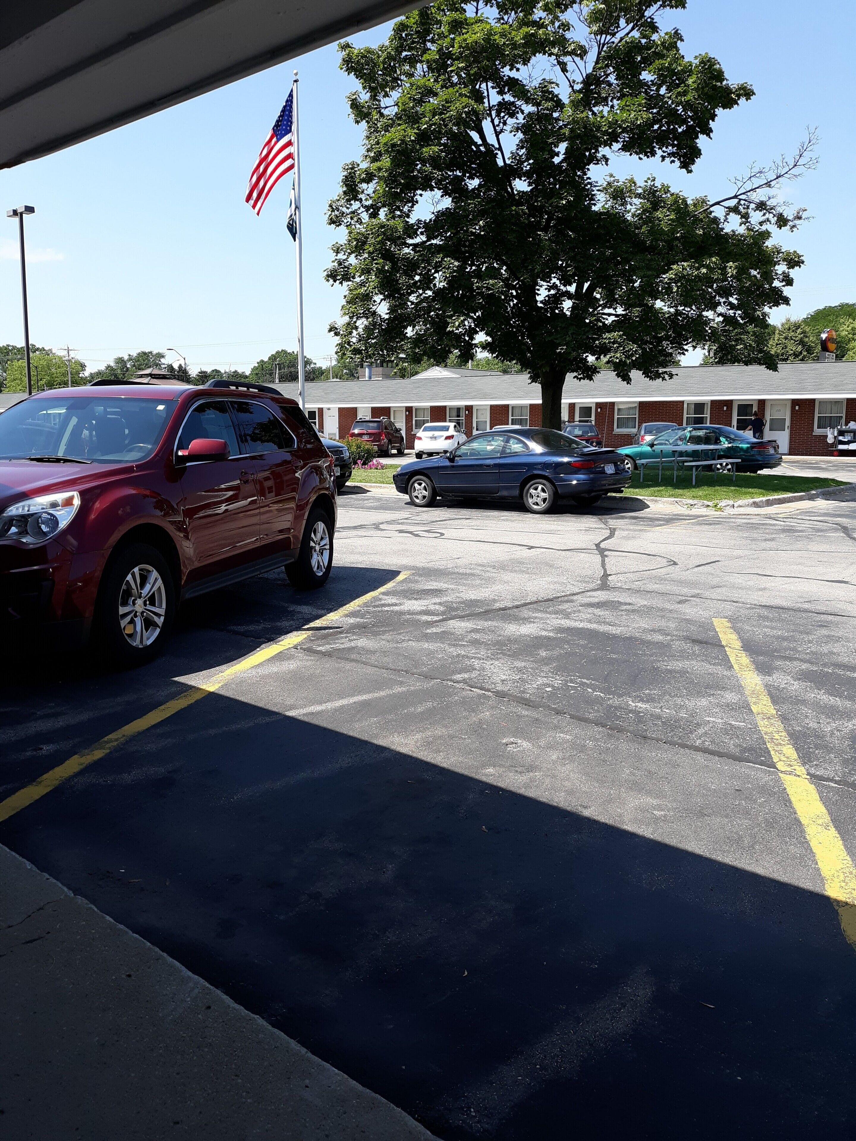 A parking lot with several cars, a large tree, and a building with a red roof in the background.