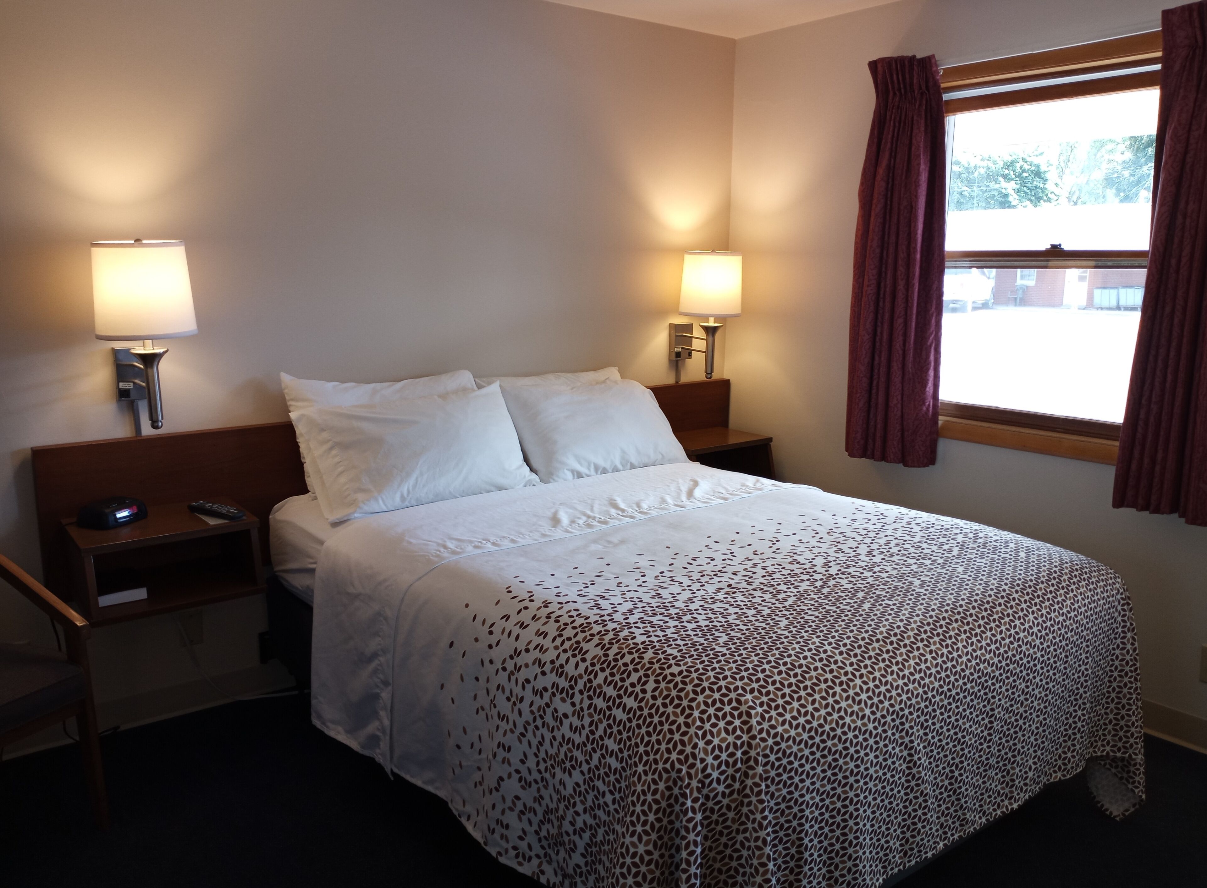 A hotel room with a bed, two bedside tables, lamps, and a window with curtains.