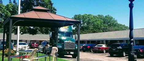 A gazebo with a flagpole, outdoor seating, and a parking lot with cars.