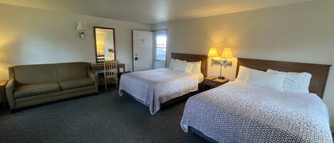 A hotel room with two beds, a sofa, a desk, and a mirror.