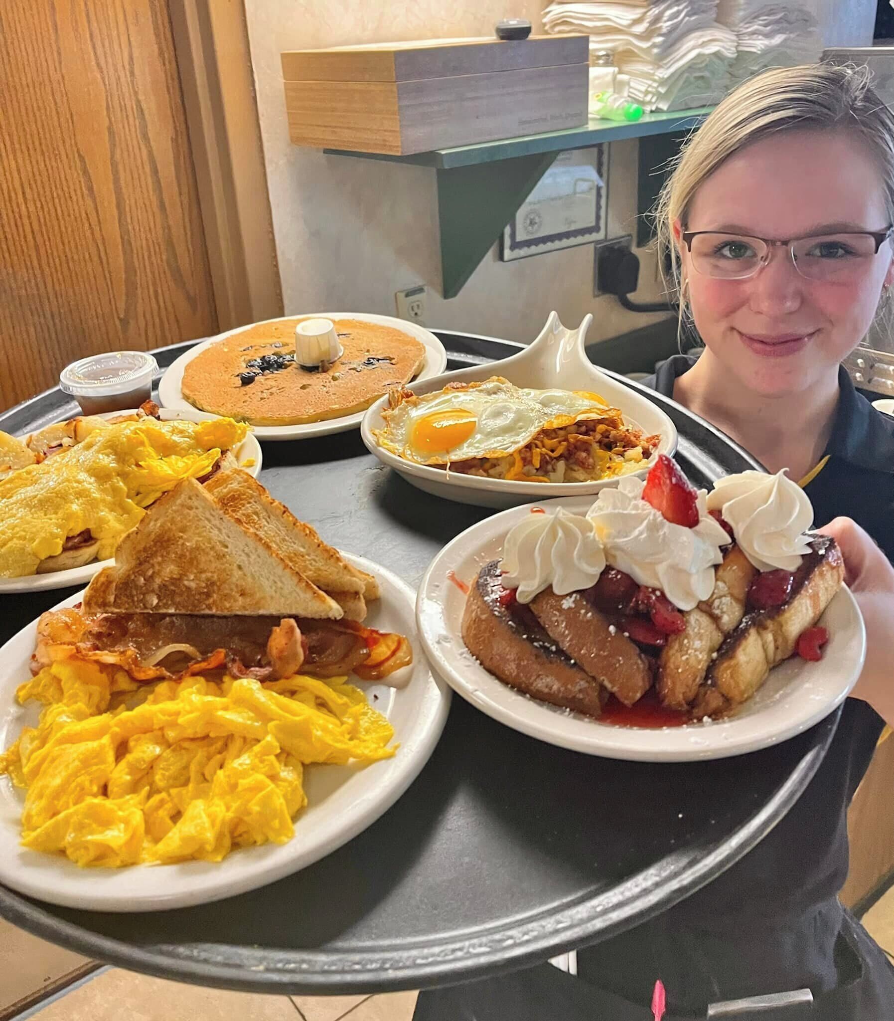 Ontbijtplateau met roerei, toast, pannenkoeken en een dessert met slagroom en bessen.