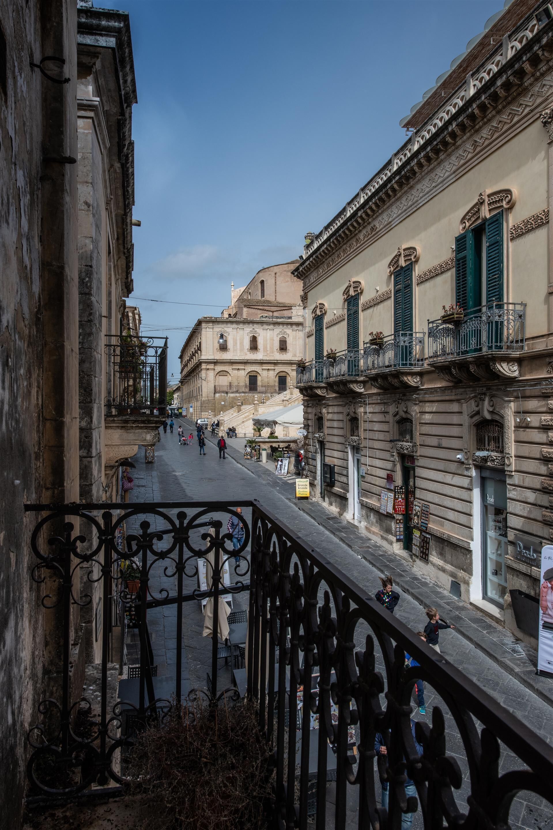 A street view with buildings, a wrought iron railing, and pedestrians.