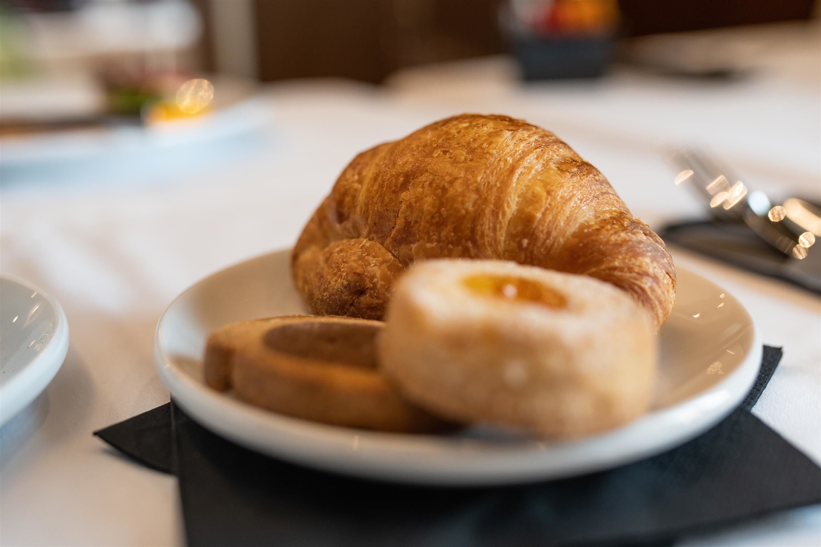 A plate with a croissant and a donut on a white tablecloth.