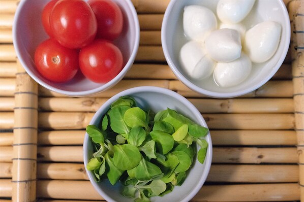 Three bowls containing tomatoes, mozzarella cheese, and leafy greens on a bamboo mat. - Hotel Porta Reale (Noto)