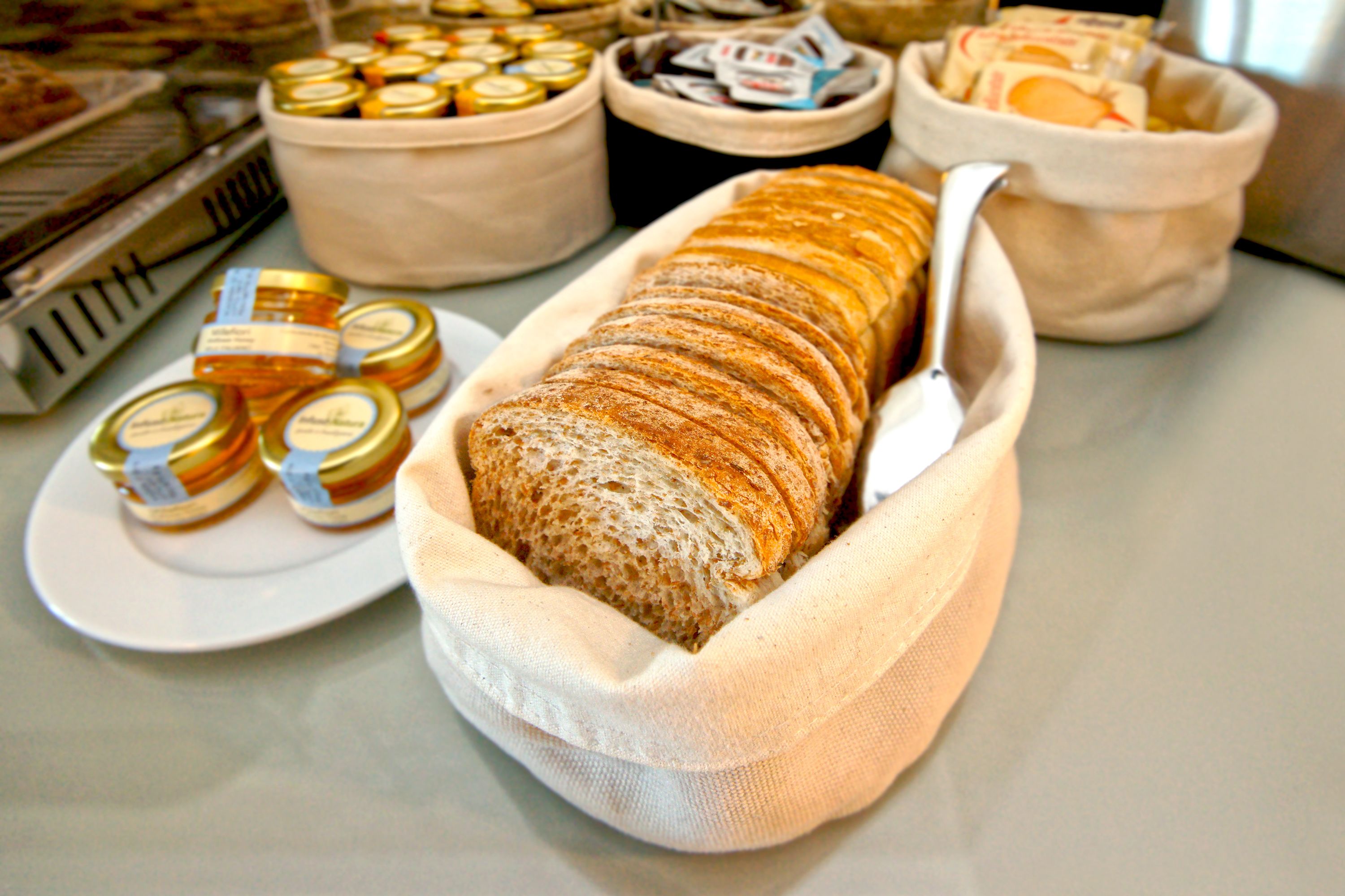 A loaf of bread in a cloth basket, surrounded by jars of honey and other food items.