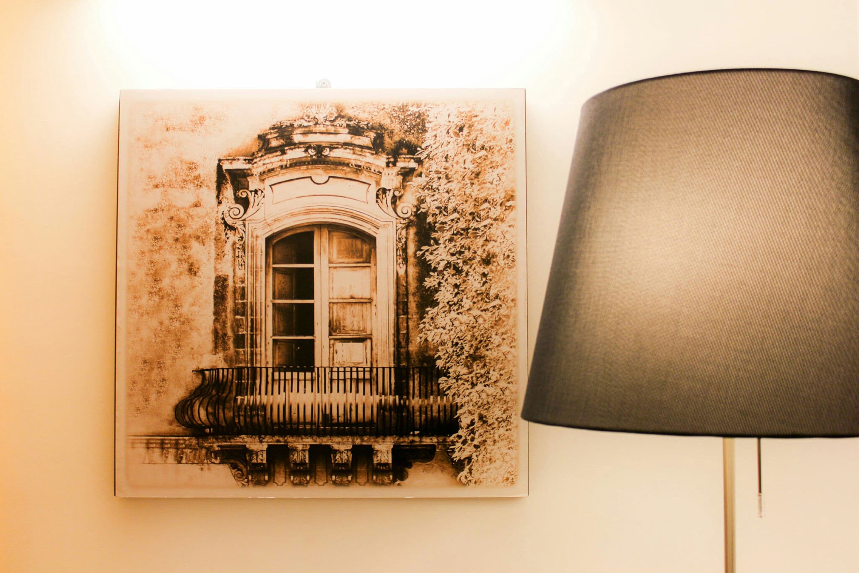 En inramad arkitektonisk ritning av en byggnad med en balkong och en lampa bredvid.