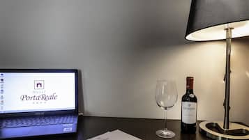 A laptop displaying a hotel booking page, a wine glass, a bottle of wine, a pen, and a notepad on a wooden table.