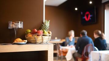 A dining area with a table set for a meal, including a basket of fruits and a glass of wine.