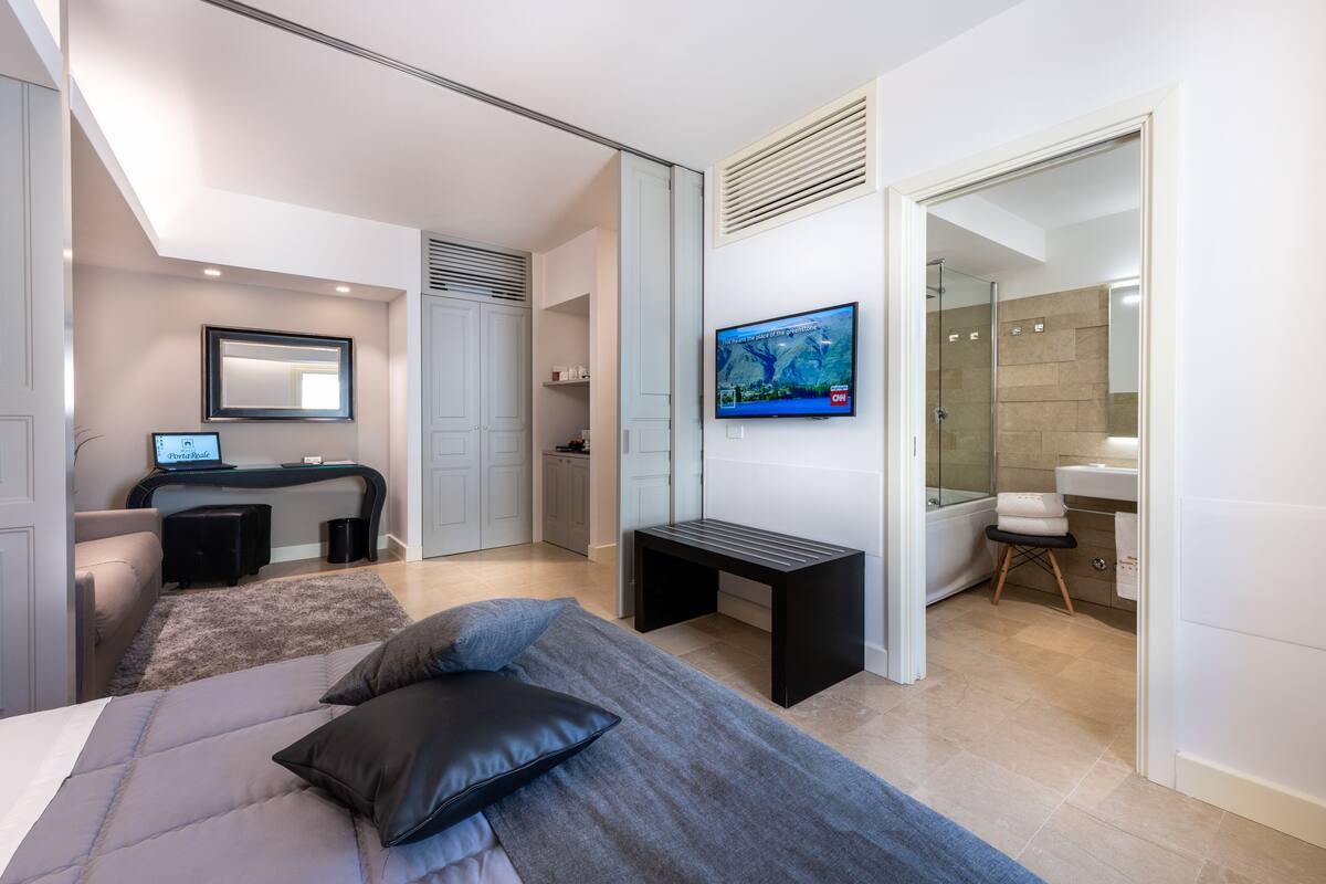 A modern bedroom with a bed, a desk, a TV, and a bathroom.